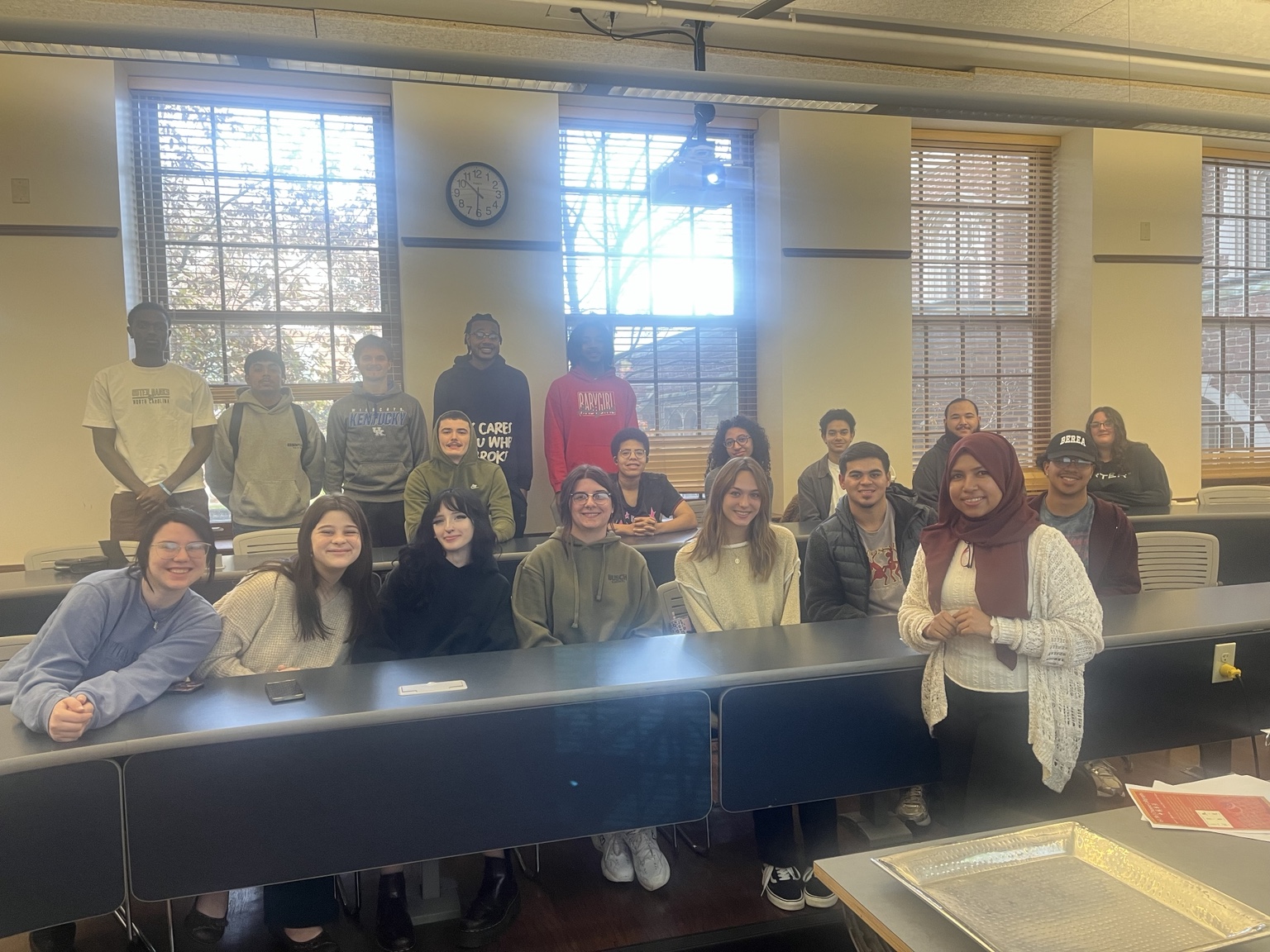 A class gathered in several rows in a bright lecture room.