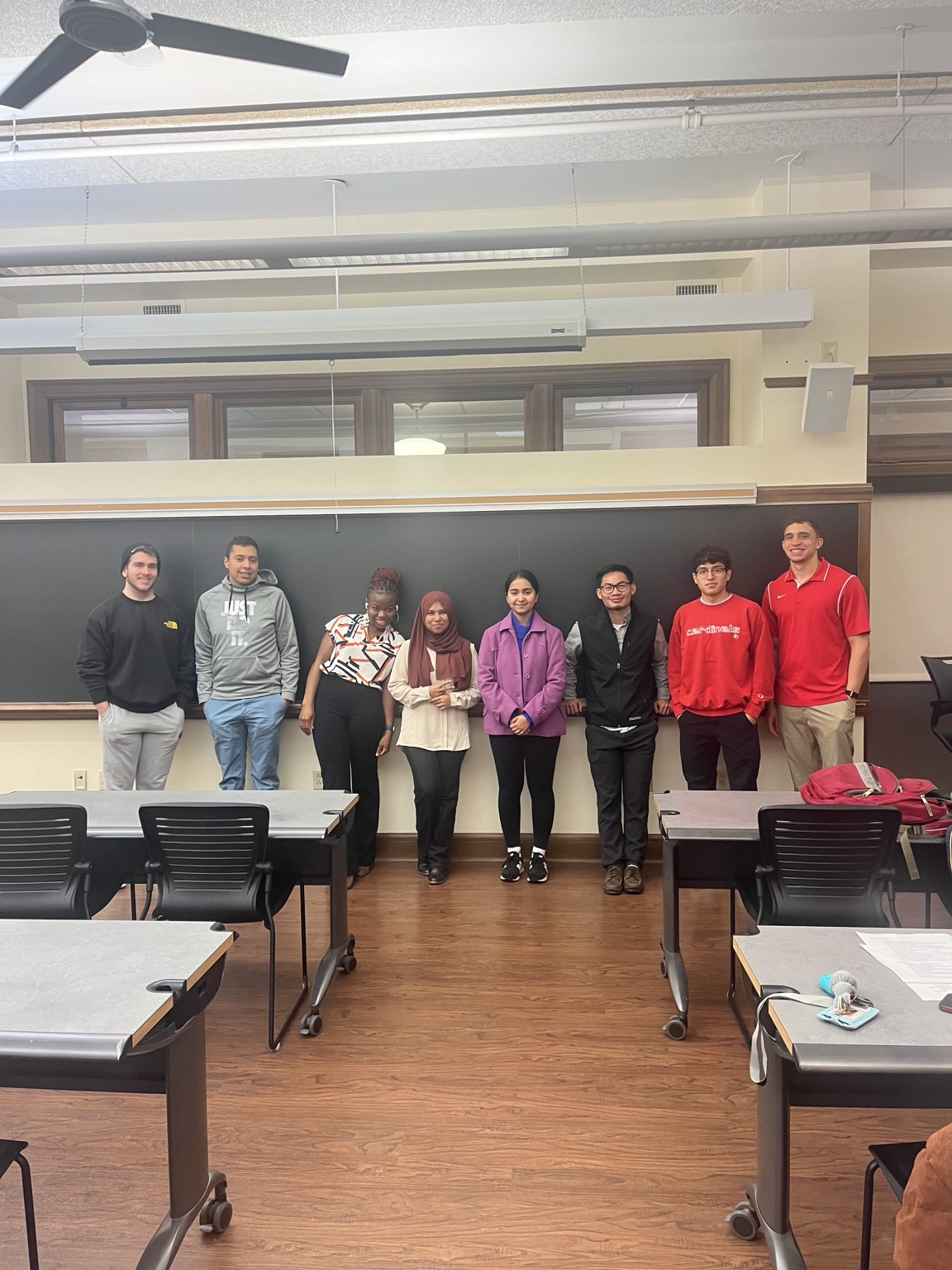 A small class standing together in front of a classroom blackboard.